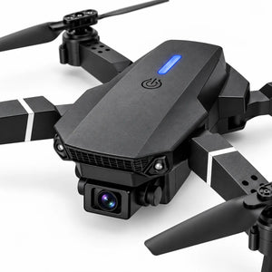 Black quadcopter drone with a mounted camera, folding arms, and a blue LED indicator light on a clean white background.