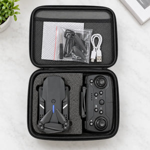 An open black hard carrying case laid on a light marble surface, showing a folded black drone inside the left compartment and a black remote controller in the right. The case interior also holds a USB cable, small accessories in a zip bag, and a white pouch.