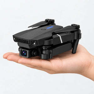 A small black foldable drone with a camera lens on the front, resting on an open hand against a clean white background.